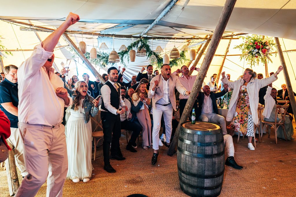 wedding guests jump up in celebration watching England score penalties in a final in a tipi