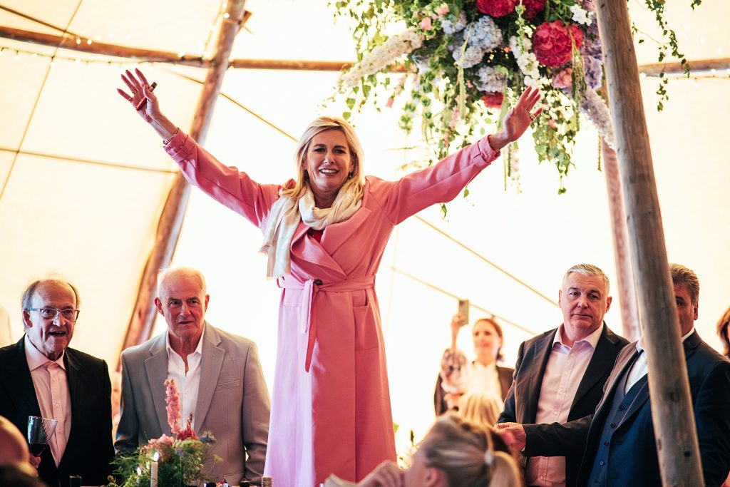 guest in pink coat stands on table with her hands in the air in a tipi