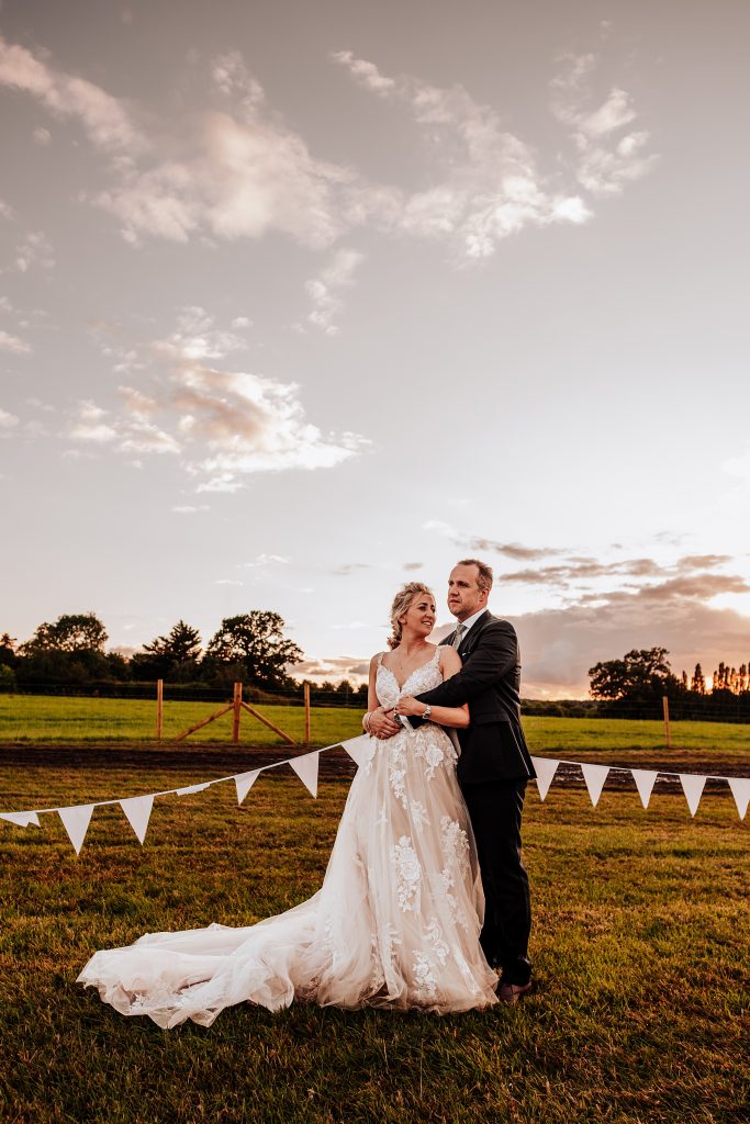 bride and groom in field with bunting at sunset