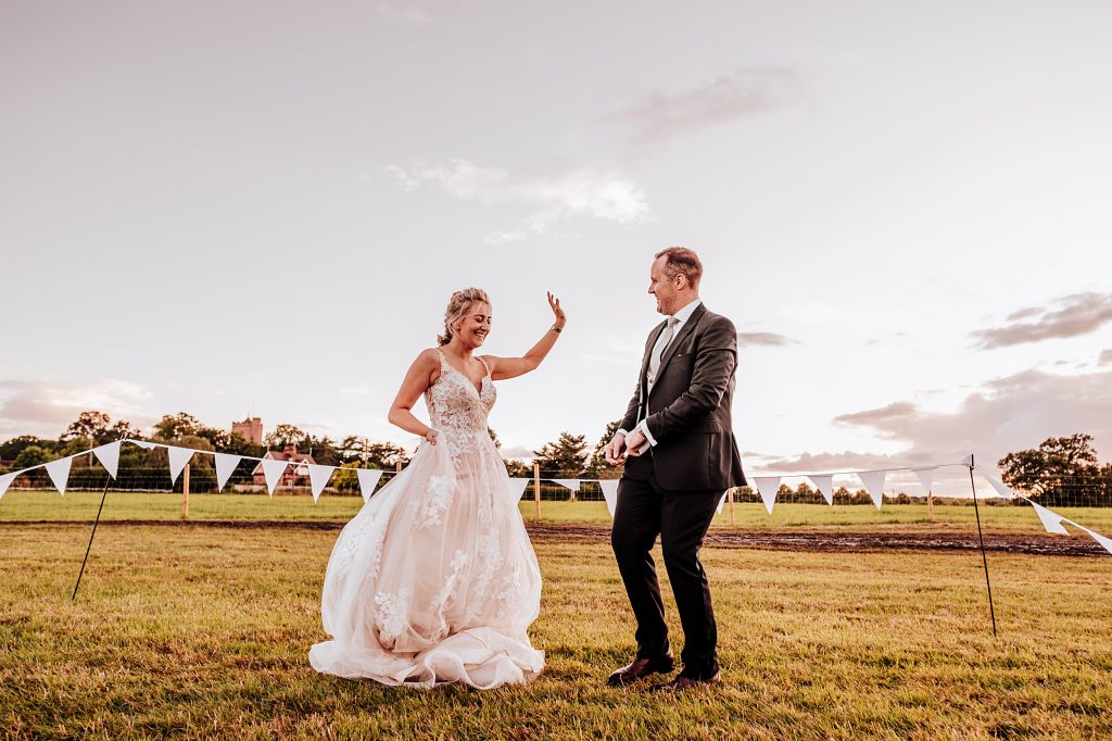 bride and groom dance in field at sunset