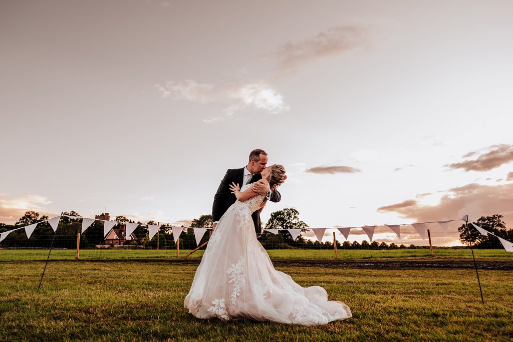 groom kisses and dips bride in field at sunset