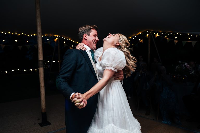 bride and groom on the dance floor, bride throws head back and laughs, fairy lights light the background