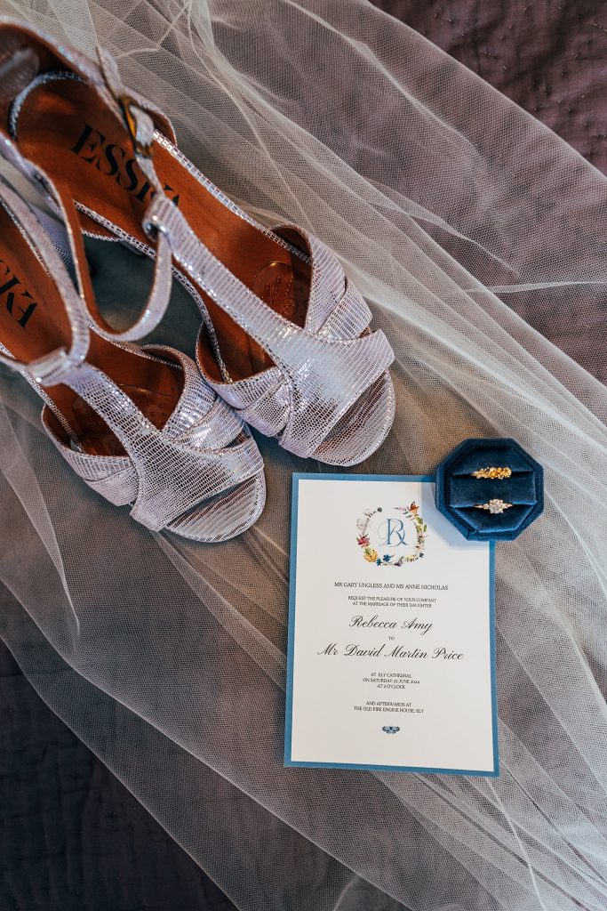 flat lay of brides shoes, veil, rings and invitation
