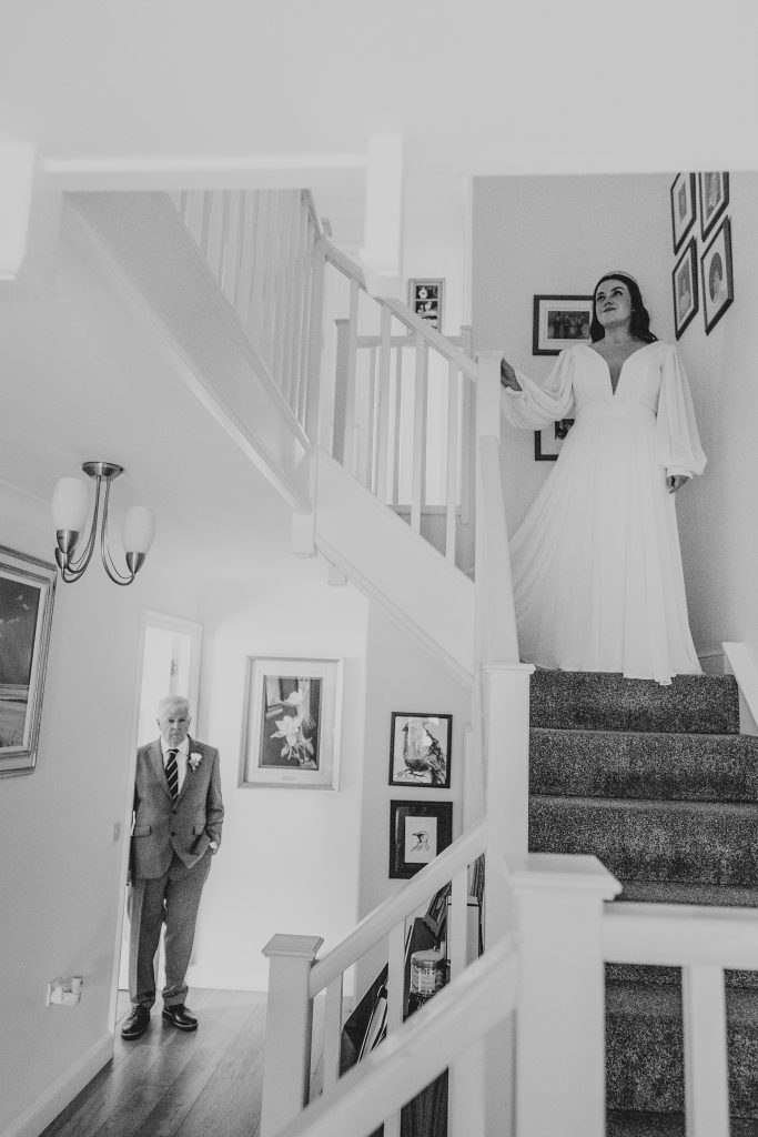 bride stands on stairwell as her dad stands in doorway at the bottom