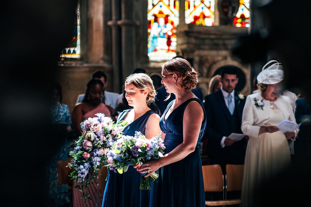 bridesmaids stand in shaft of sunlight Ely Cathedral