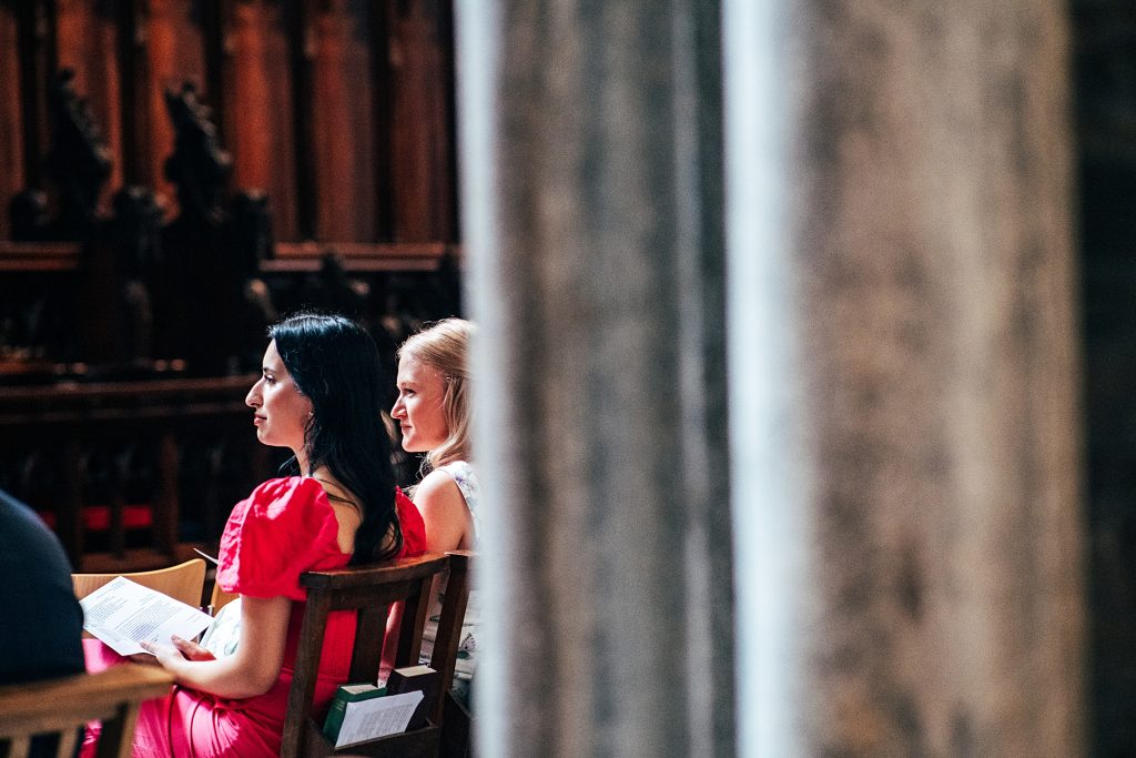 two wedding guests listen to reading Ely Cathedral
