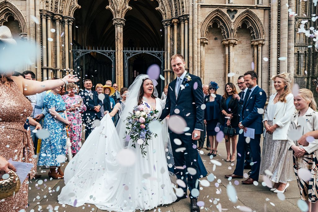 guests throw confetti on couple outside Ely Cathedral