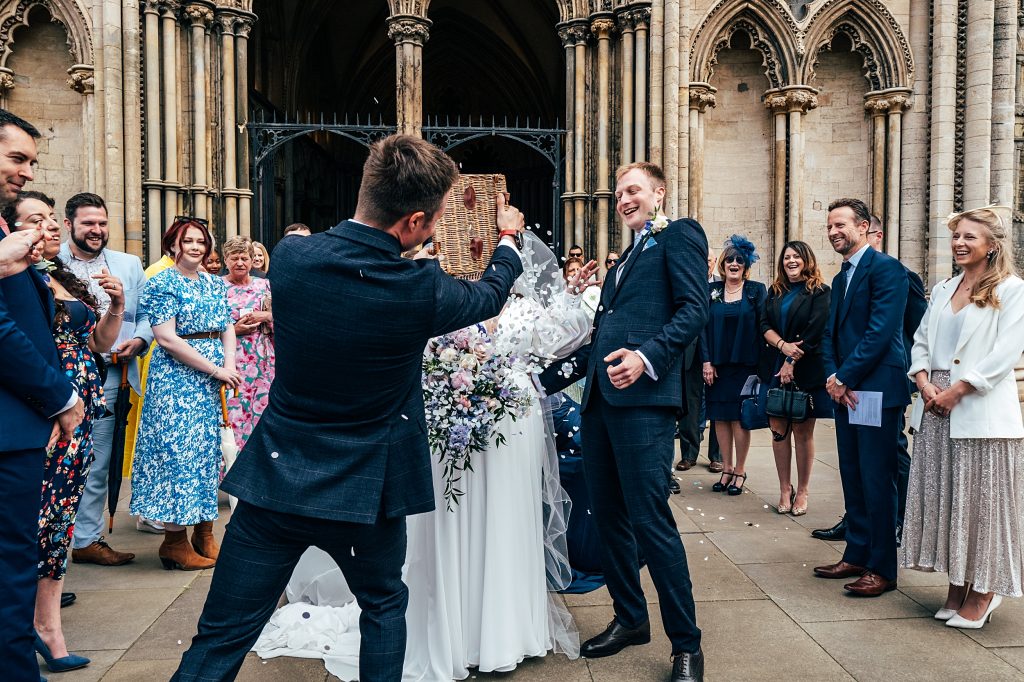 guests throw confetti on couple outside Ely Cathedral
