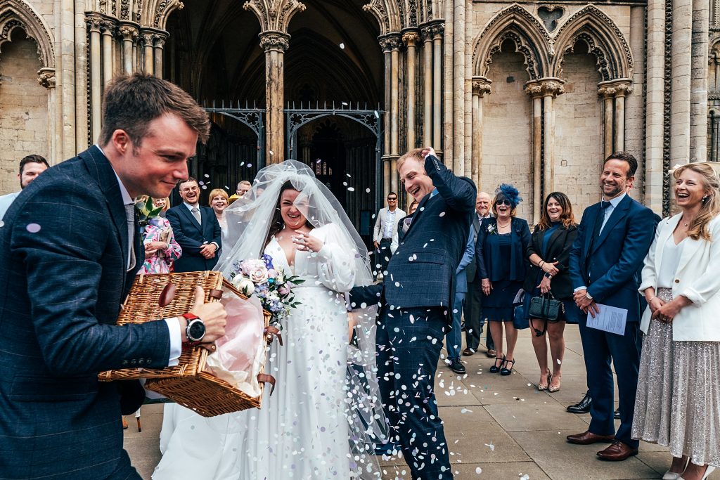 guests throw confetti on couple outside Ely Cathedral