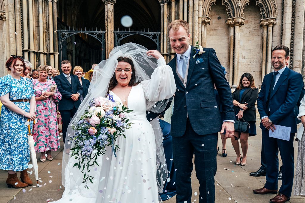 guests throw confetti on couple outside Ely Cathedral