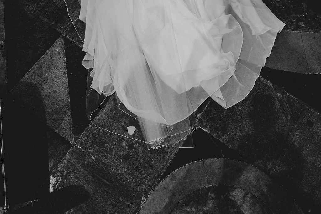 single heart shaped confetti stuck in brides veil as she walks tiled floor at Ely Cathedral