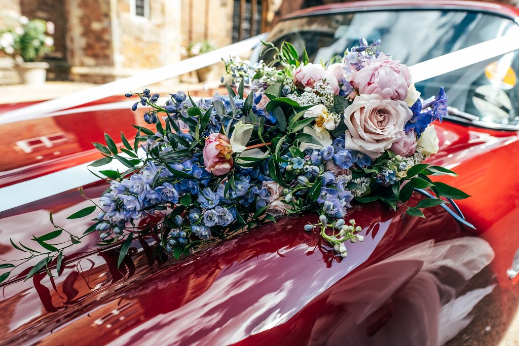 brides bouquet on bonnet of red sports car