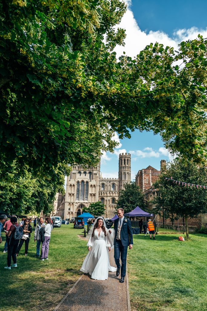 bride and groom walk away from Ely Cathedral