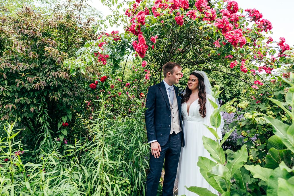 bride and groom under pink rose arch