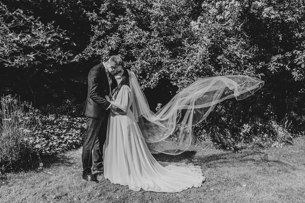 bride and groom kiss as her veil billows behind her