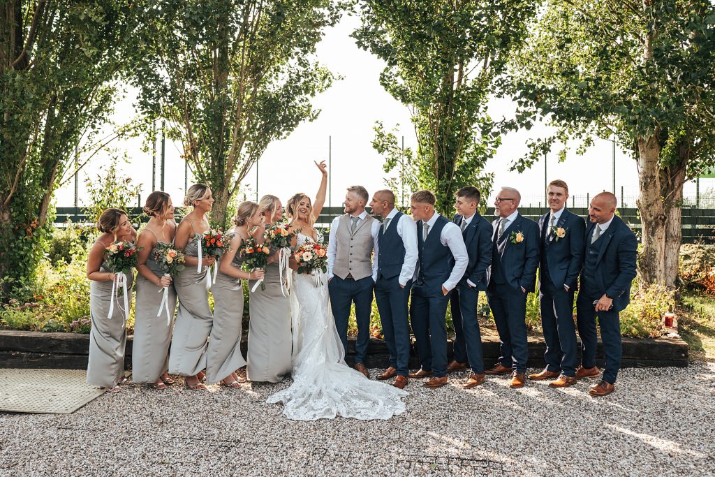 bride lifts arm in air as groom and wedding party look at her
