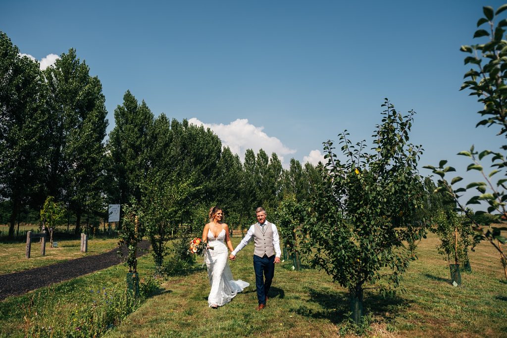 bride and groom stroll hand in hand through tree line