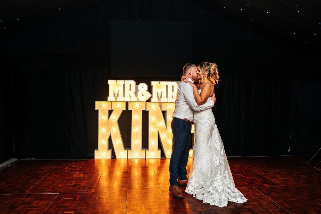 bride and groom first dance on dance floor lit by marquee lights of their new name