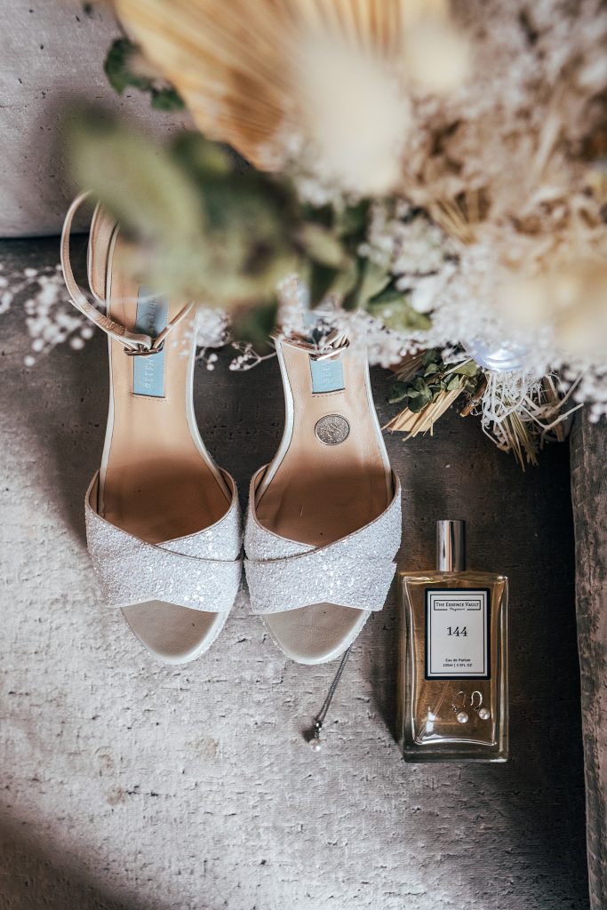 brides shoes, perfume, earrings with bouquet in foreground