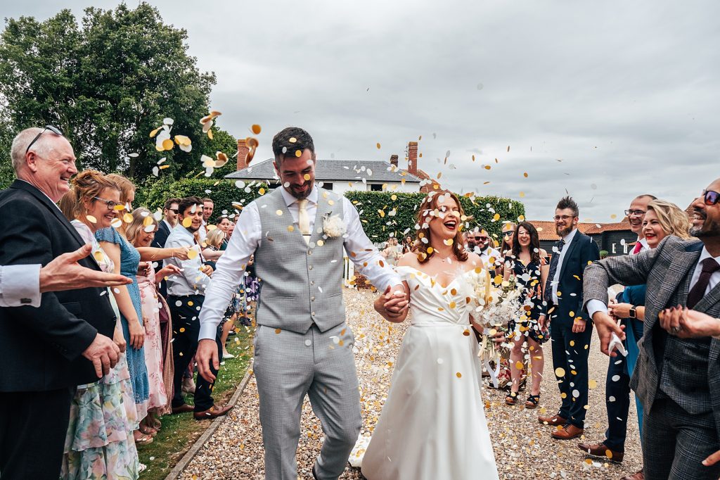 bride and groom laugh as they walk confetti tunnel