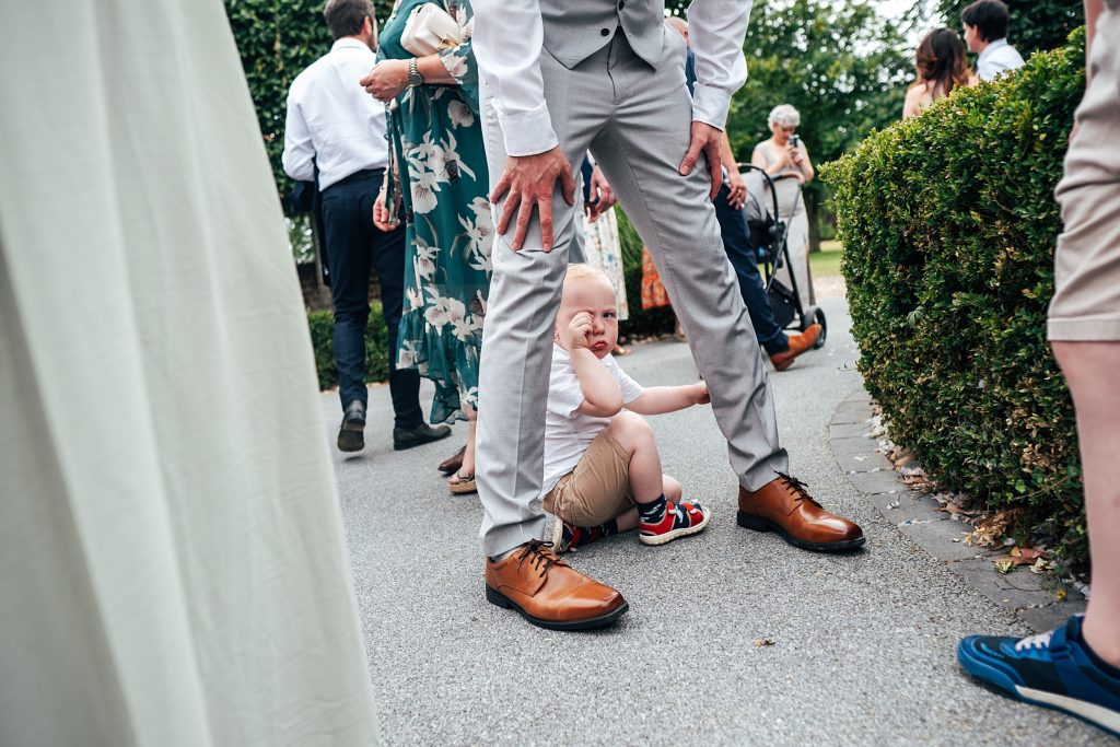 little boy rubs face as he peers from between dads legs