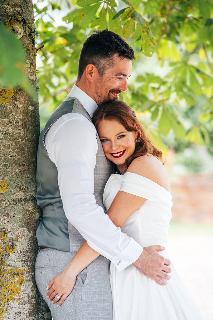 smiling bride and groom hug under a tree