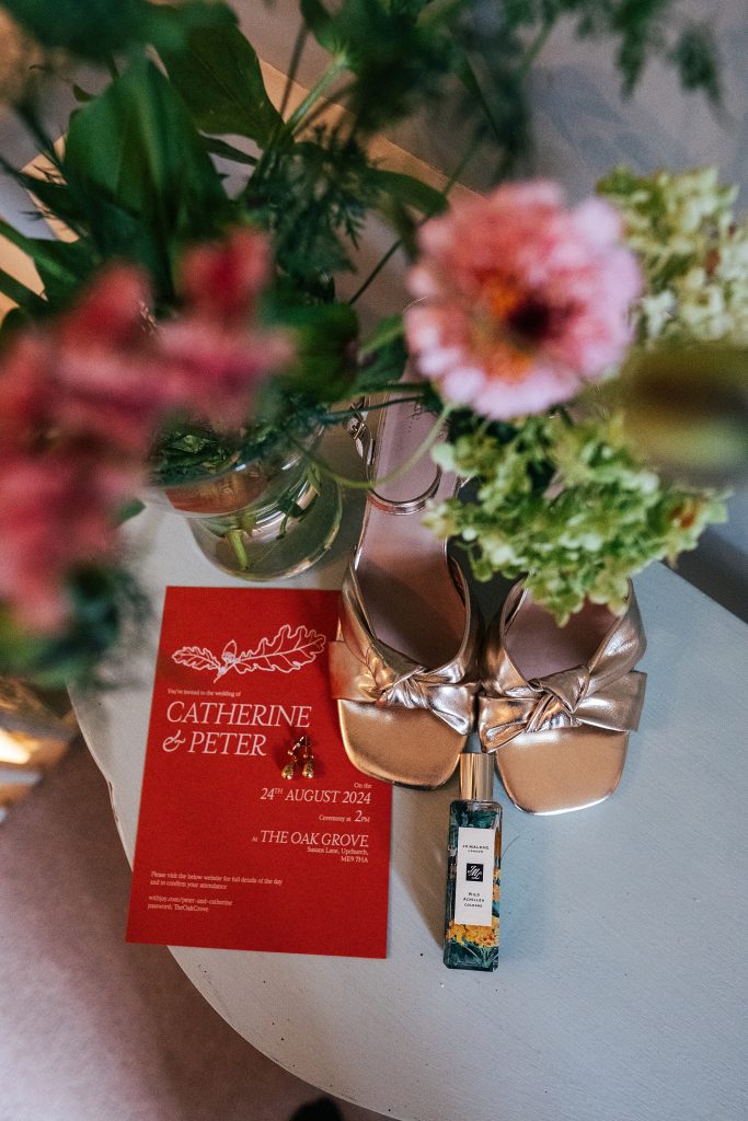 Flat lay of brides shoes, perfume, earrings and invitation with flowers in the foreground