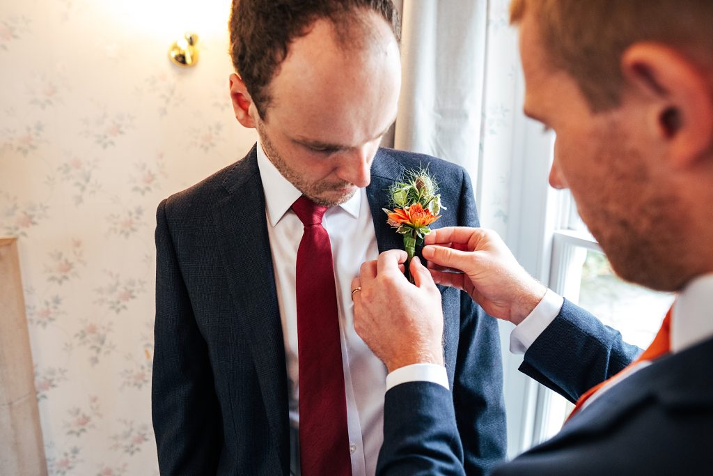 best man helps groom with his button hole