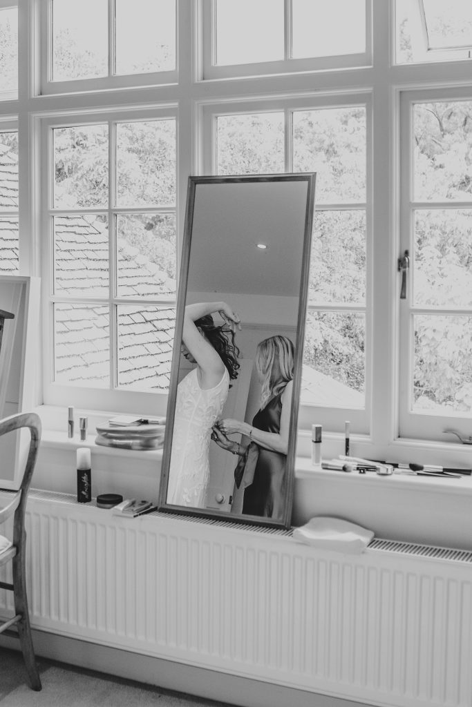 bridesmaid does up brides dress reflection in mirror