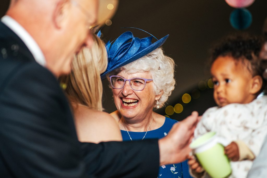wedding guest in blue hat laughs at another guest