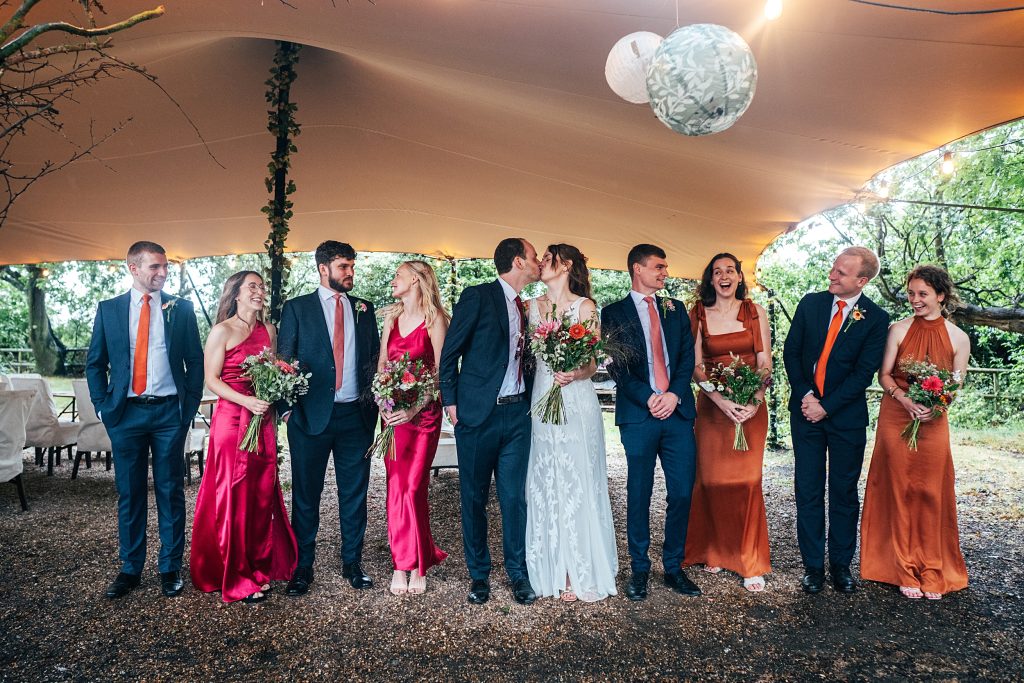 bride, groom and wedding party in pinks and oranges under a stretch canopy