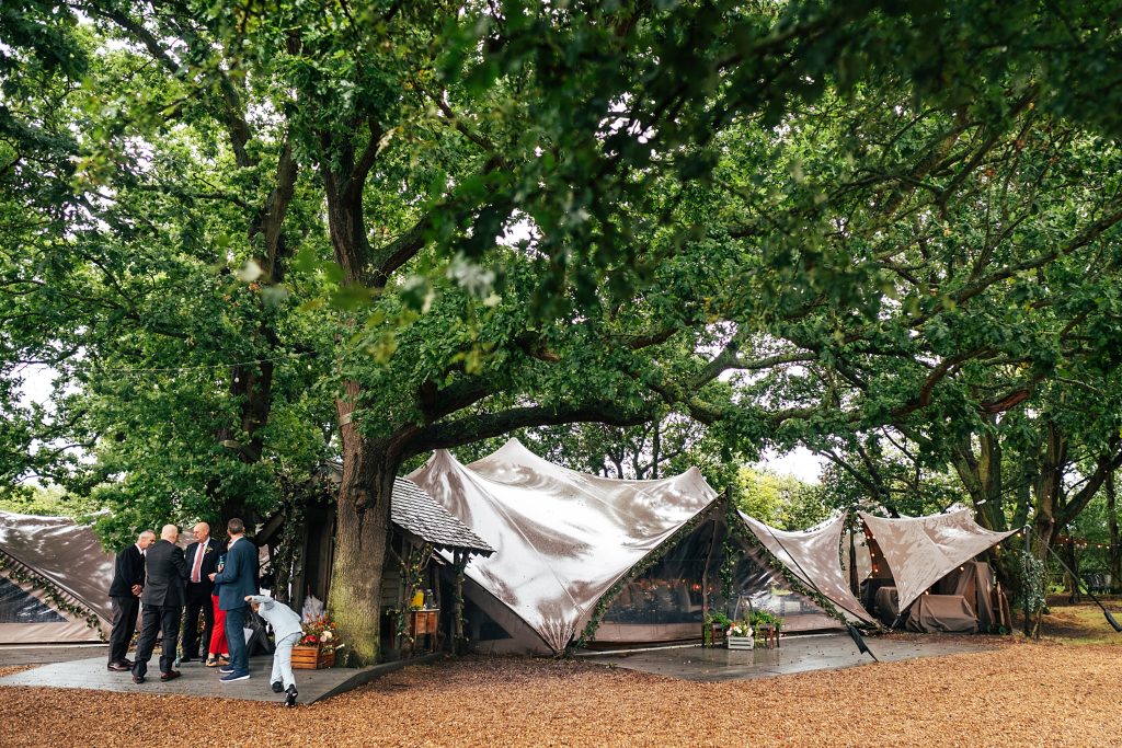 a few wedding guests brave the rain and stand outside a stretch tent wedding venue