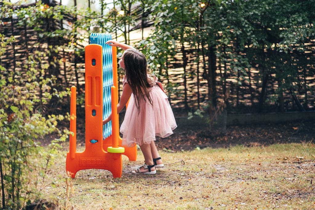 little girl in pink dress plays garden connect 4