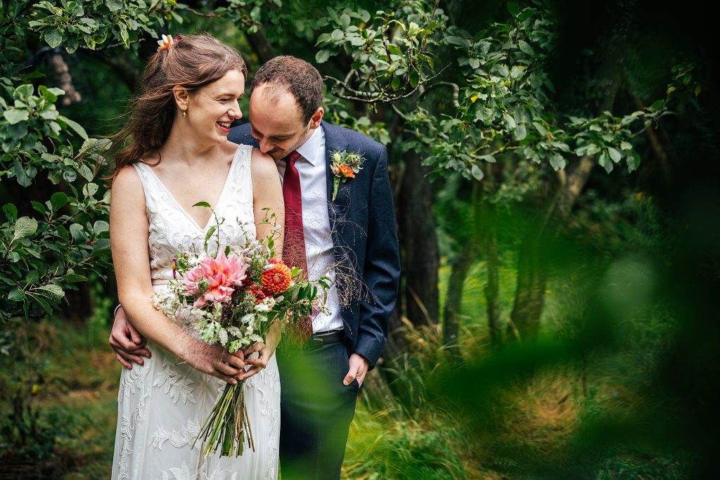groom kisses brides shoulder amongst an orchard