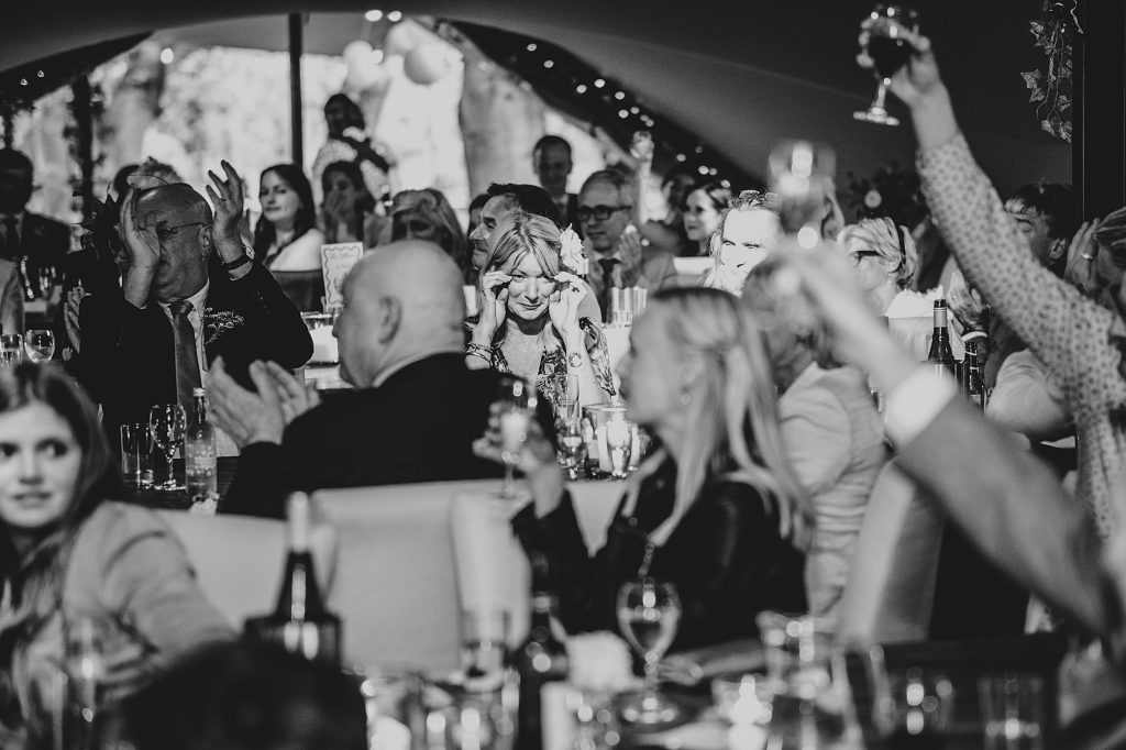 spotlight on crying wedding guests as others raise toasts and clap in stretch tent