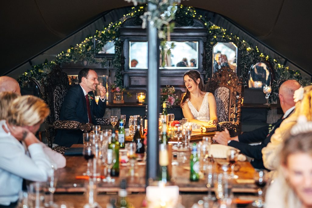 bride and groom laugh during speech in stretch tent