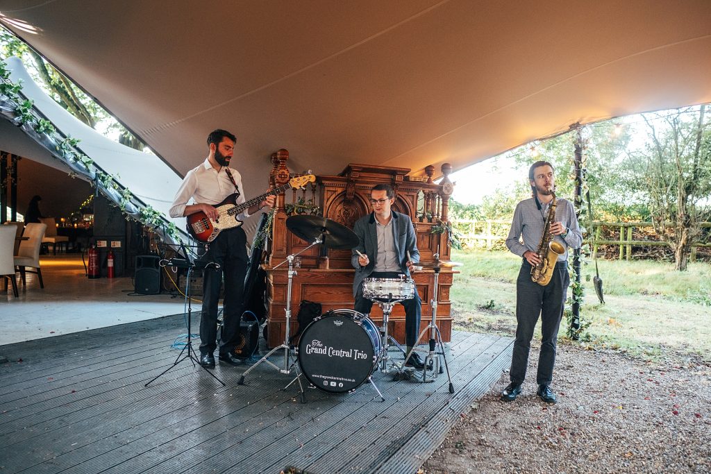 three piece folk band play under a stretch canopy