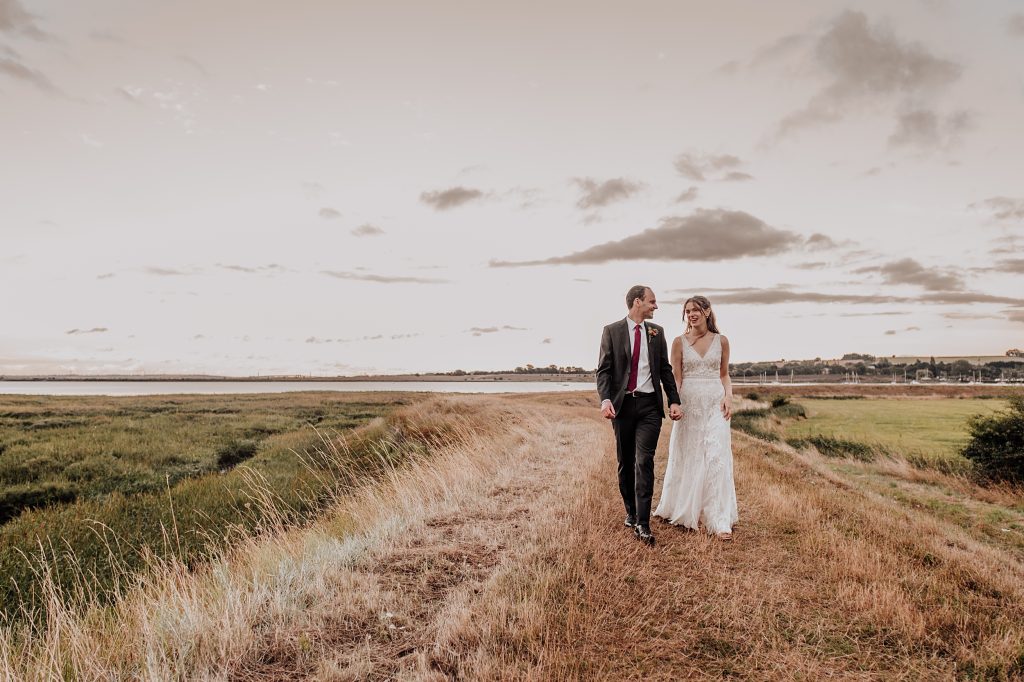 bride and groom walk along grassy headland near coast at sunset
