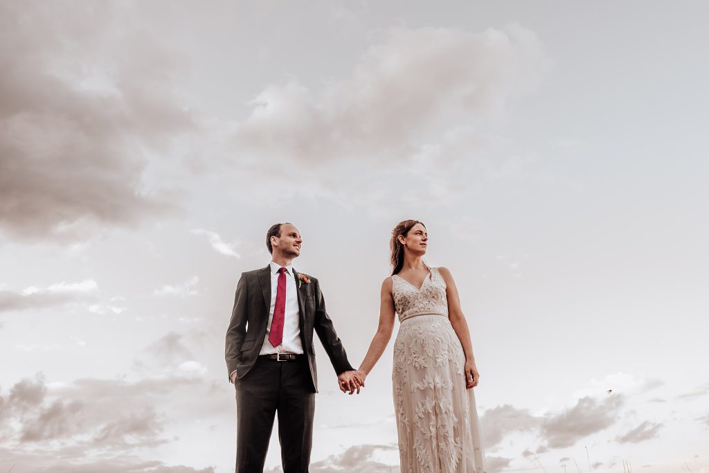 bride and groom hold hands against cloudy evening sky