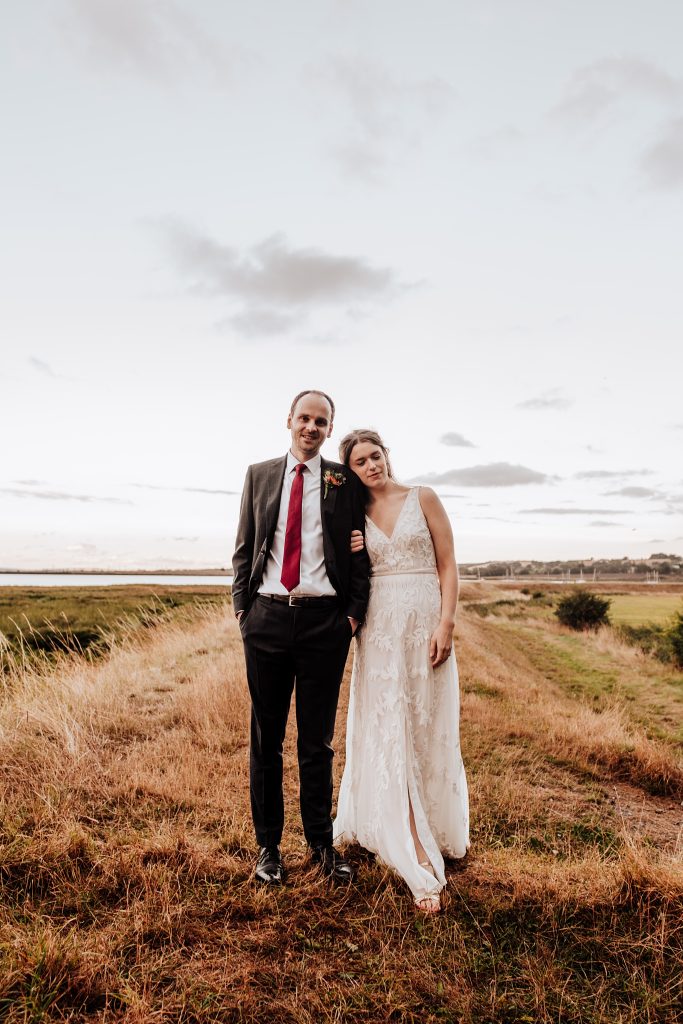 bride leans on grooms shoulder on headland under evening sky