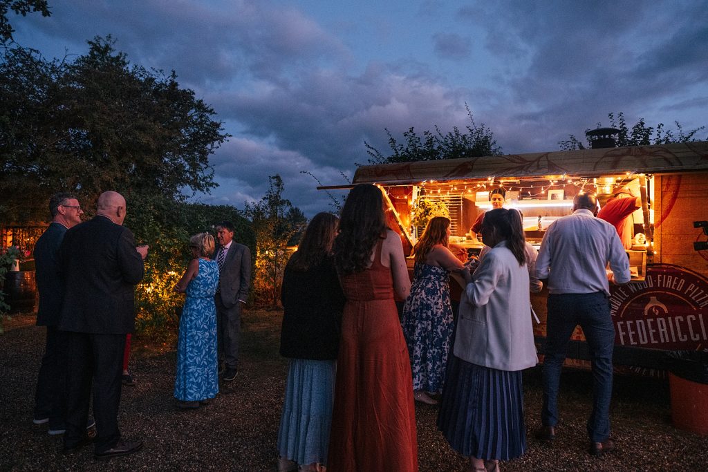 wedding guests at a pizza truck under dusky sky