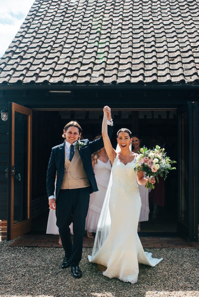 bride and groom hold up hands in triumph as they leave ceremony