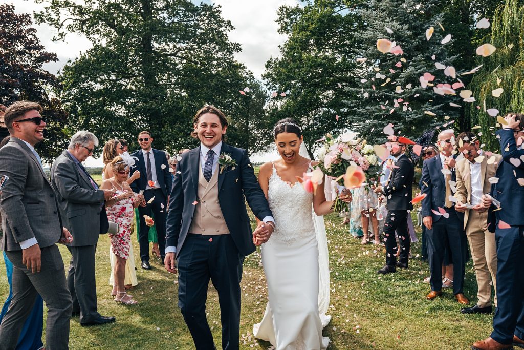 smiling bride and groom walk confetti tunnel