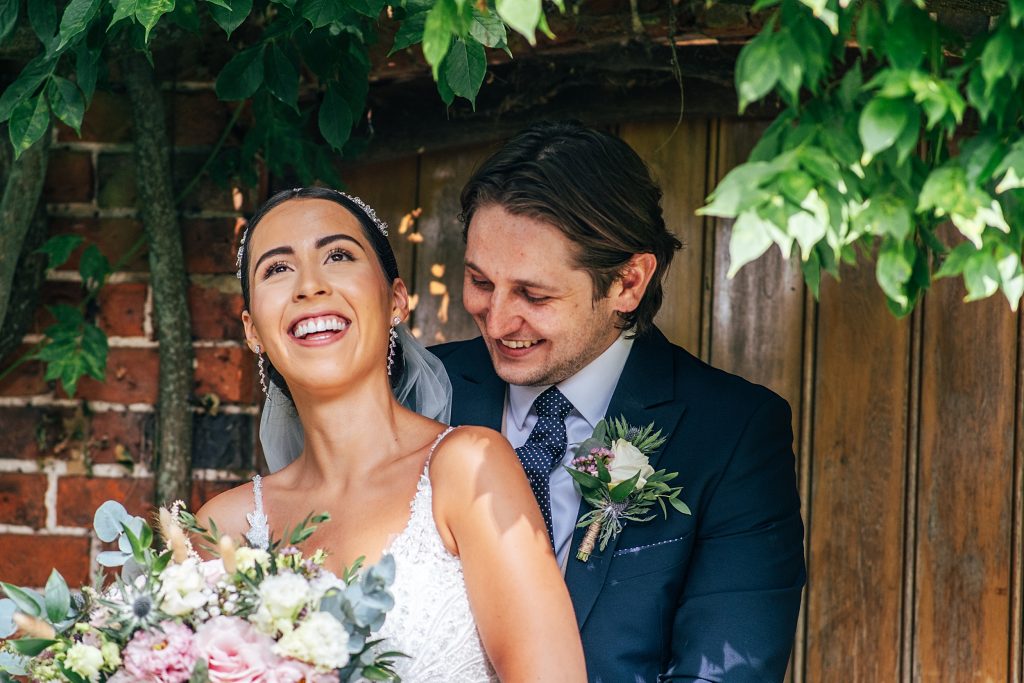 bride and groom laugh as they stand in doorway in gardens