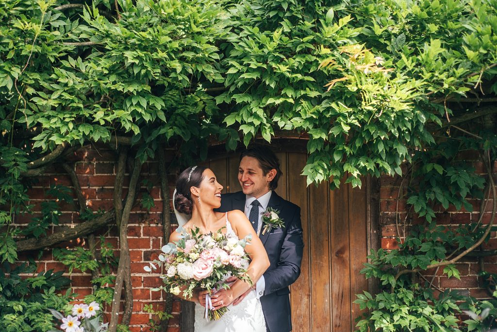 bride and groom laugh in doorway of walled gardens