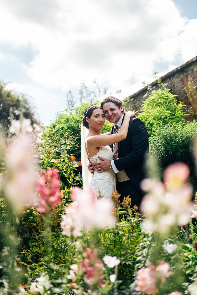bride and groom in lush gardens with pink flowers in foreground