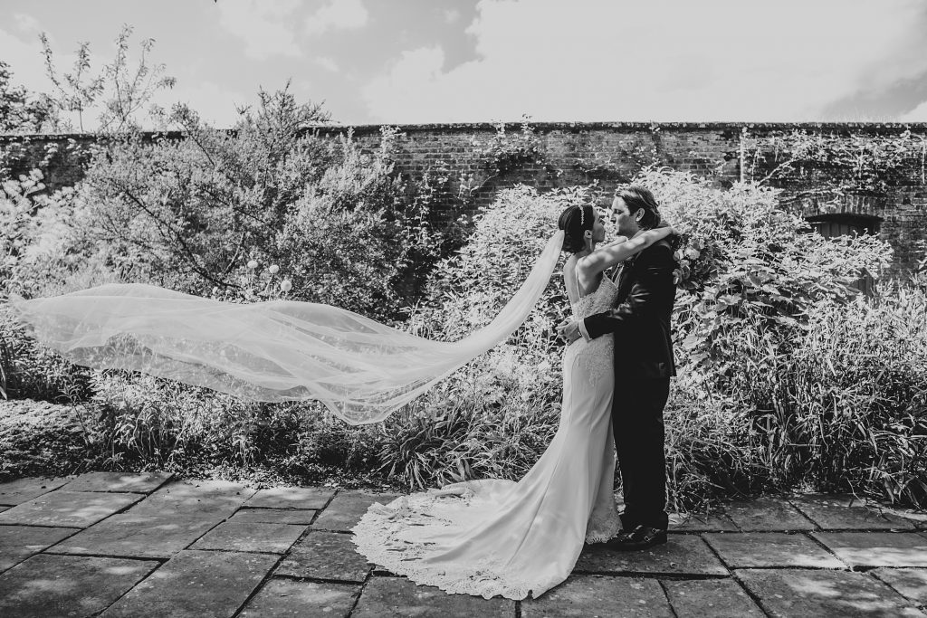 bride and groom kiss in gardens as veil billows out behind