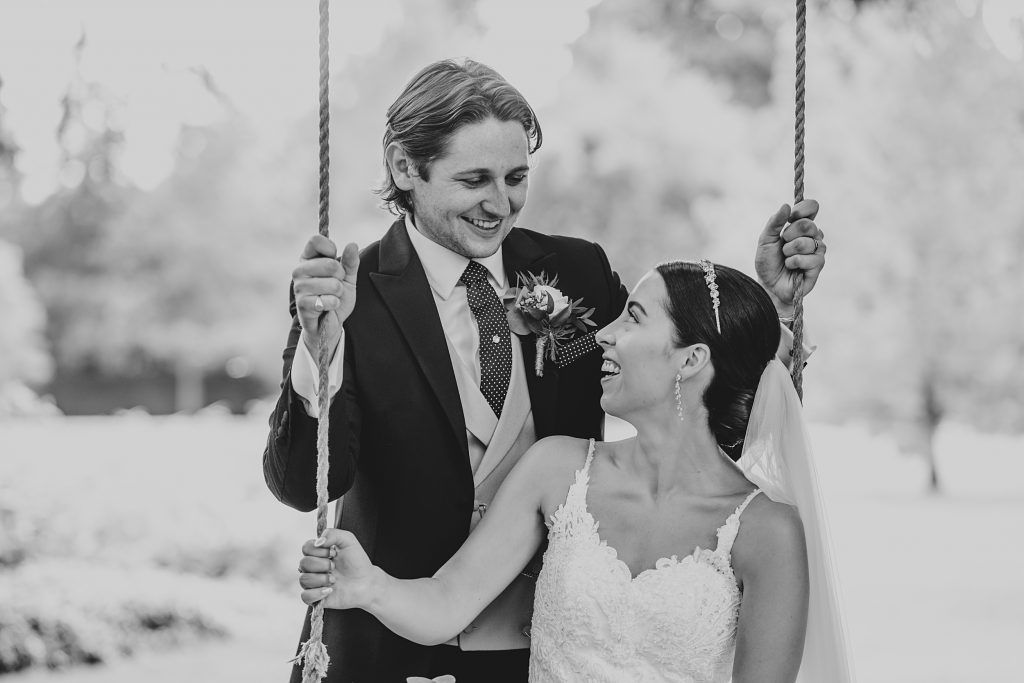 bride sits on swing with groom behind her