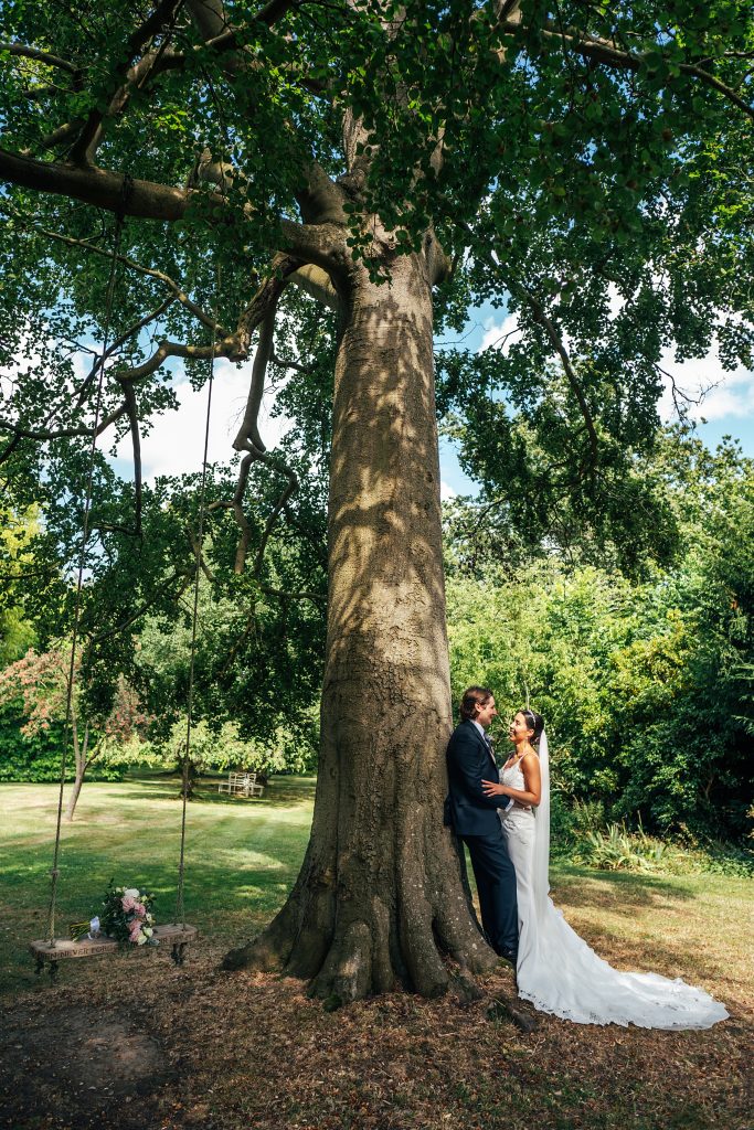 bride and groom stand under huge oak tree with a swing hanging from it