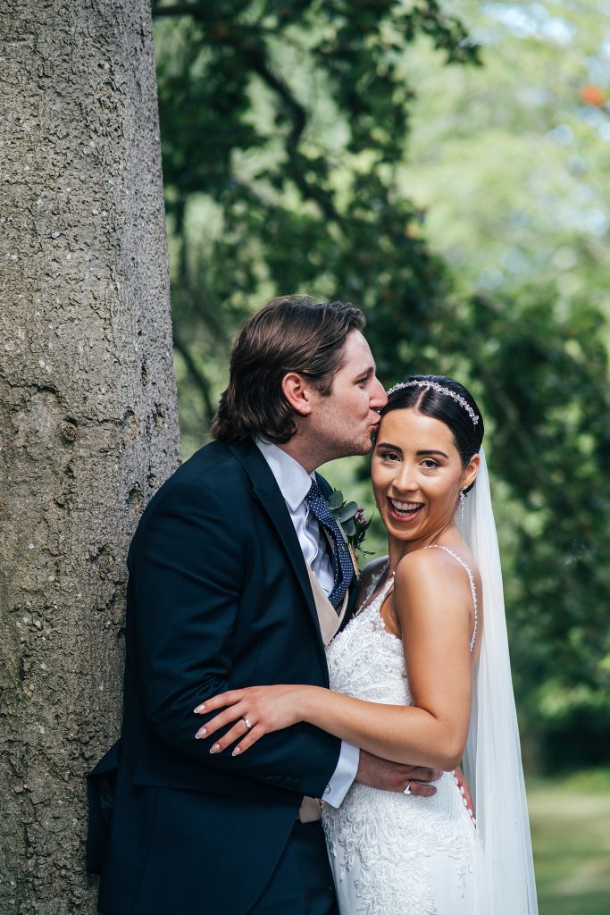 bride laughs as groom kisses head under oak tree
